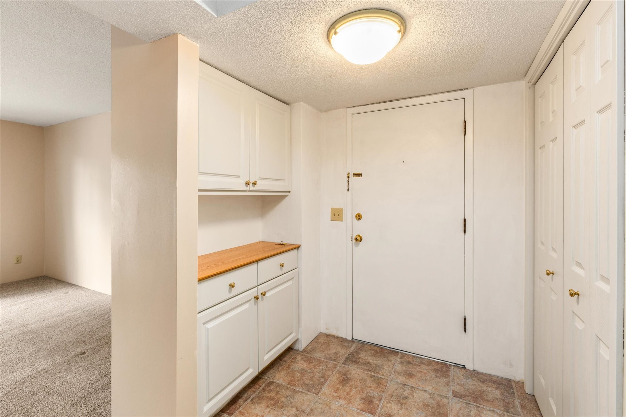 Entryway with built-in white cabinets, a wood countertop, brown tile floor, and white front door.