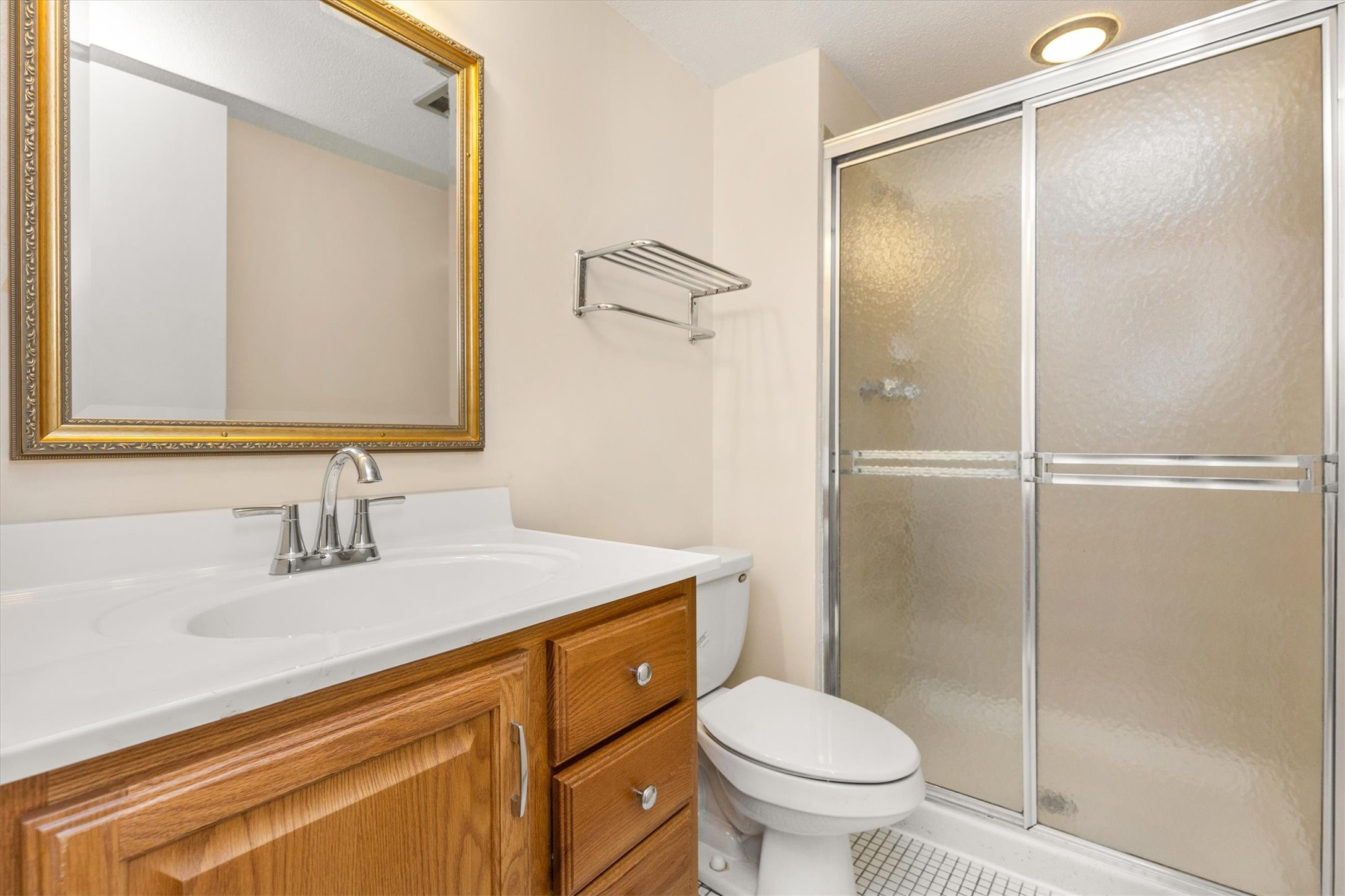 Bathroom with a wood vanity, framed mirror, toilet, and frosted-glass shower.