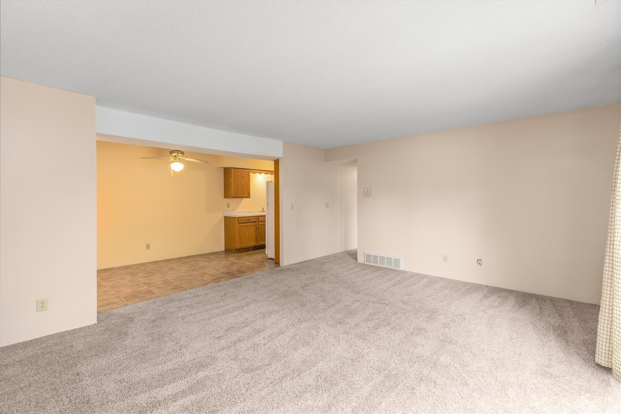 Unfurnished living room with gray carpet and an open view into the tiled kitchen and dining area.