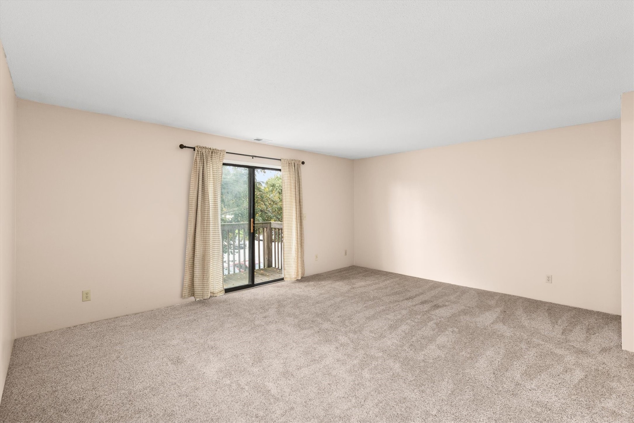 Empty carpeted room with a curtained sliding glass door opening onto a balcony.