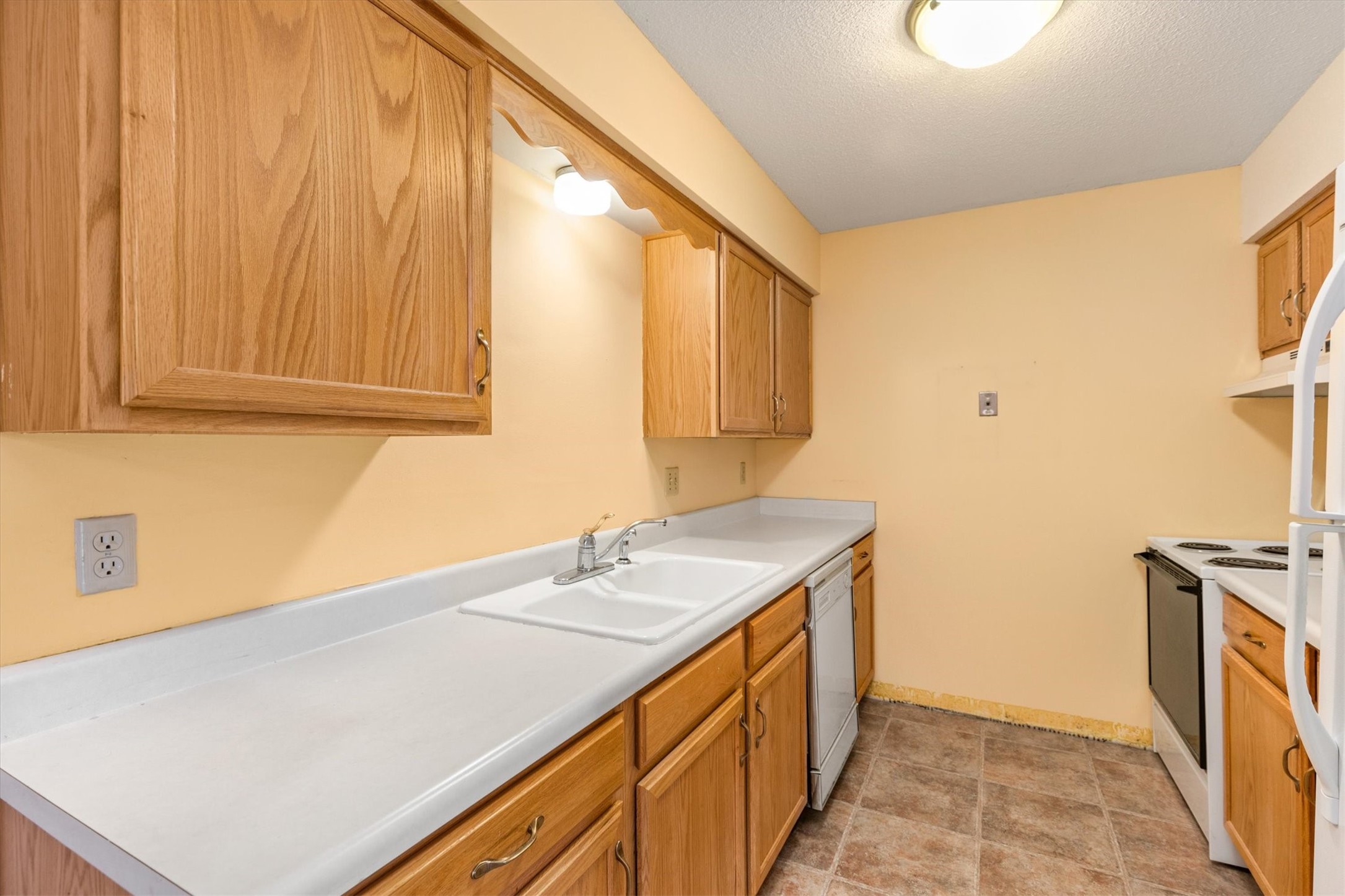 Kitchen with oak cabinets, white counters, double sink, dishwasher, and electric range.