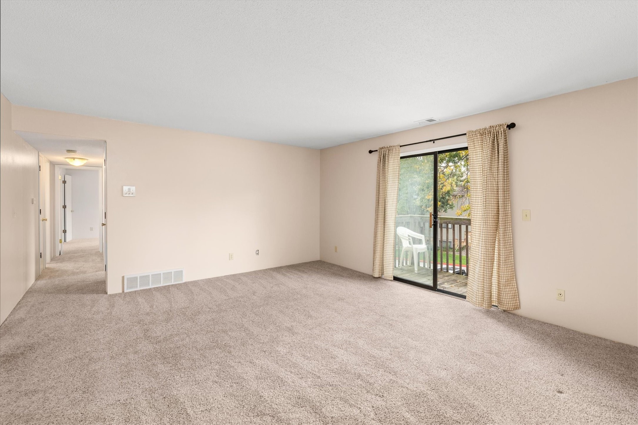 Unfurnished living room with beige carpet and a sliding glass door opening onto a deck.