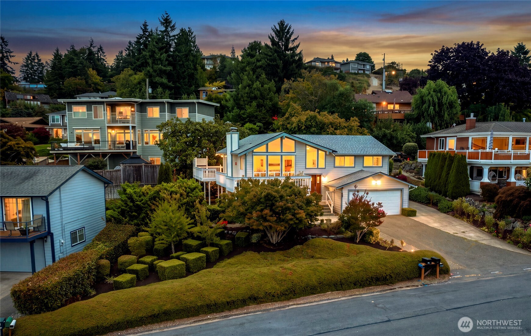 Light-blue two-story home with a gabled window wall and attached garage glowing at dusk.