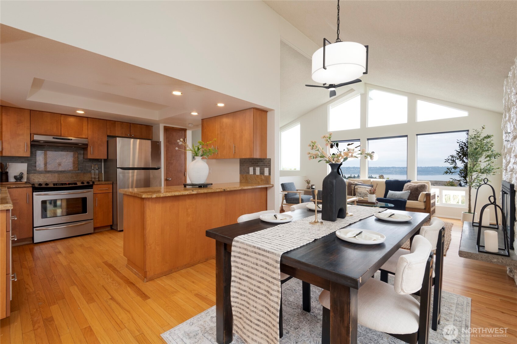 Open-plan kitchen and dining room with warm wood cabinetry and tall windows overlooking the water.