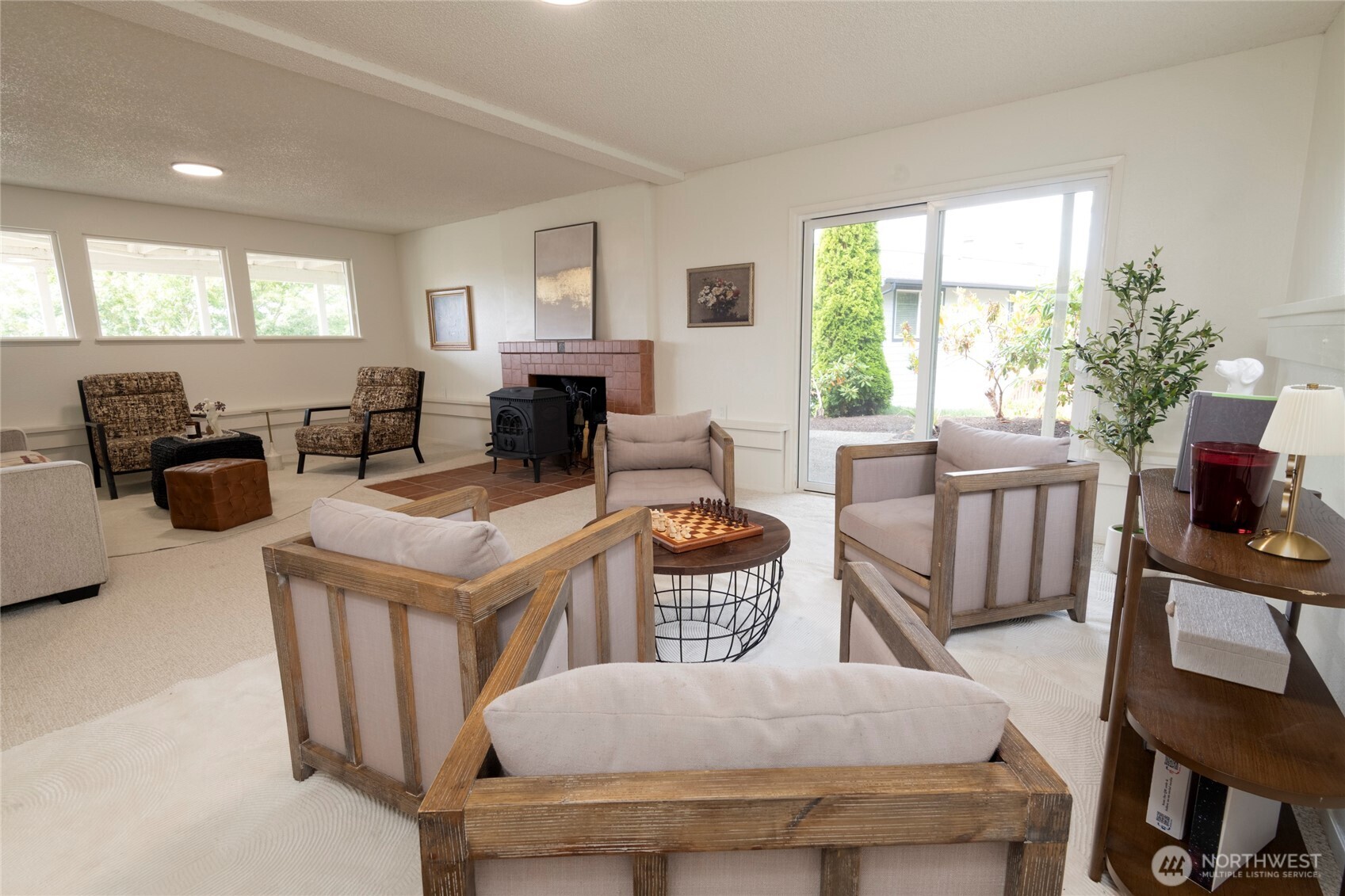 Staged living room with a tiled fireplace, freestanding wood stove, and sliding glass door to the yard.