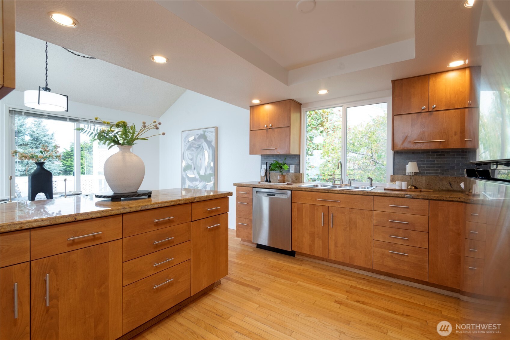 Kitchen with warm wood cabinets, granite island, stainless steel dishwasher, and hardwood floors.