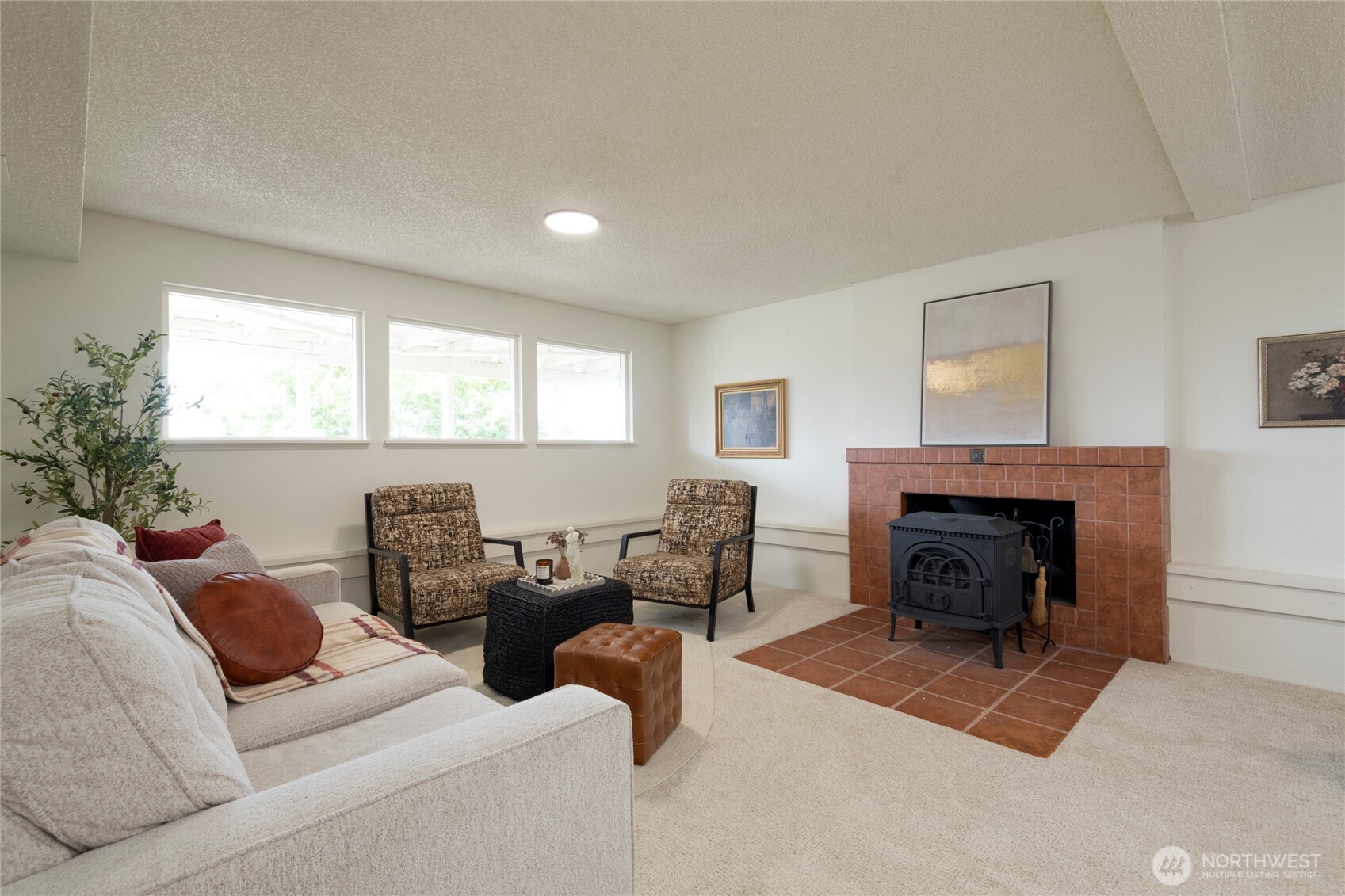 Living room with a tiled fireplace, black wood stove, and three high windows.
