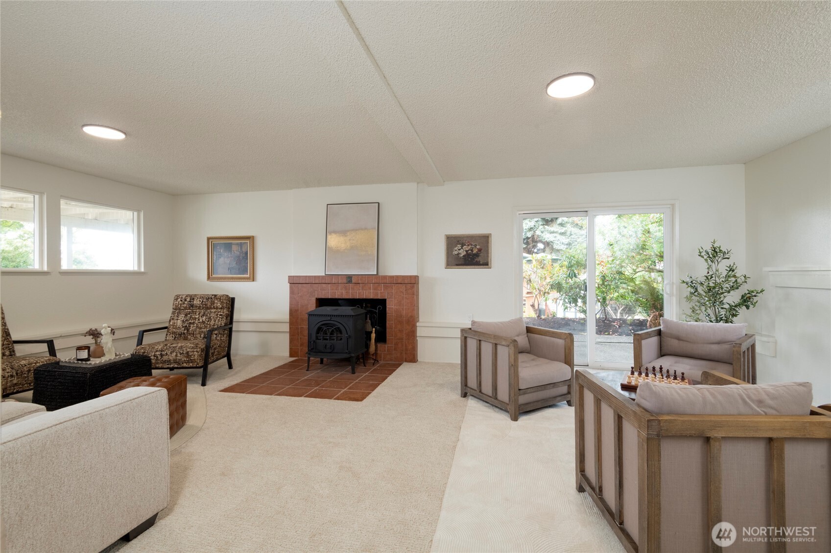 Furnished living room with a tiled fireplace, black wood stove, and sliding glass door to the yard.