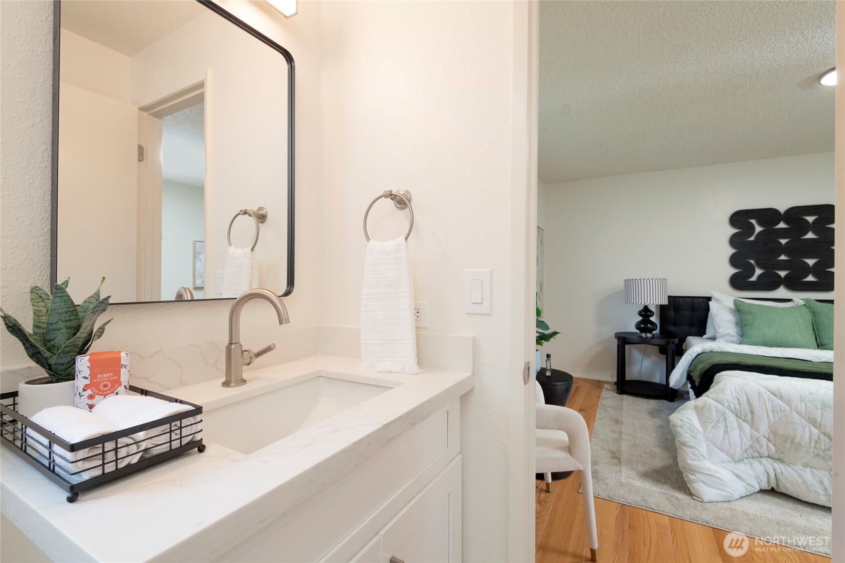 Bathroom vanity with marble-look counter and mirror, looking through an open doorway into a bedroom with green accents.