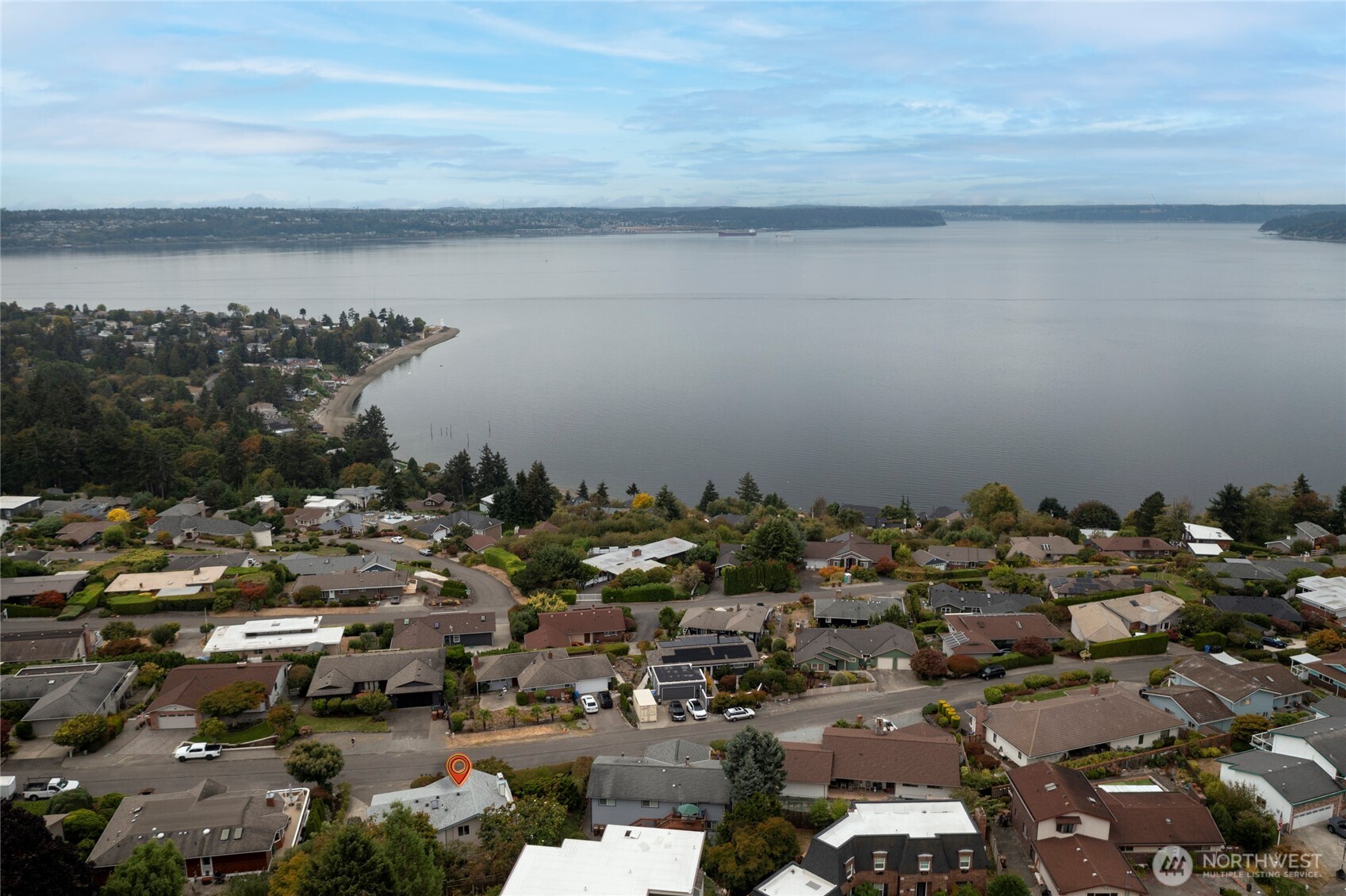 Aerial view of a waterfront neighborhood, with a location marker over a home beside the bay.