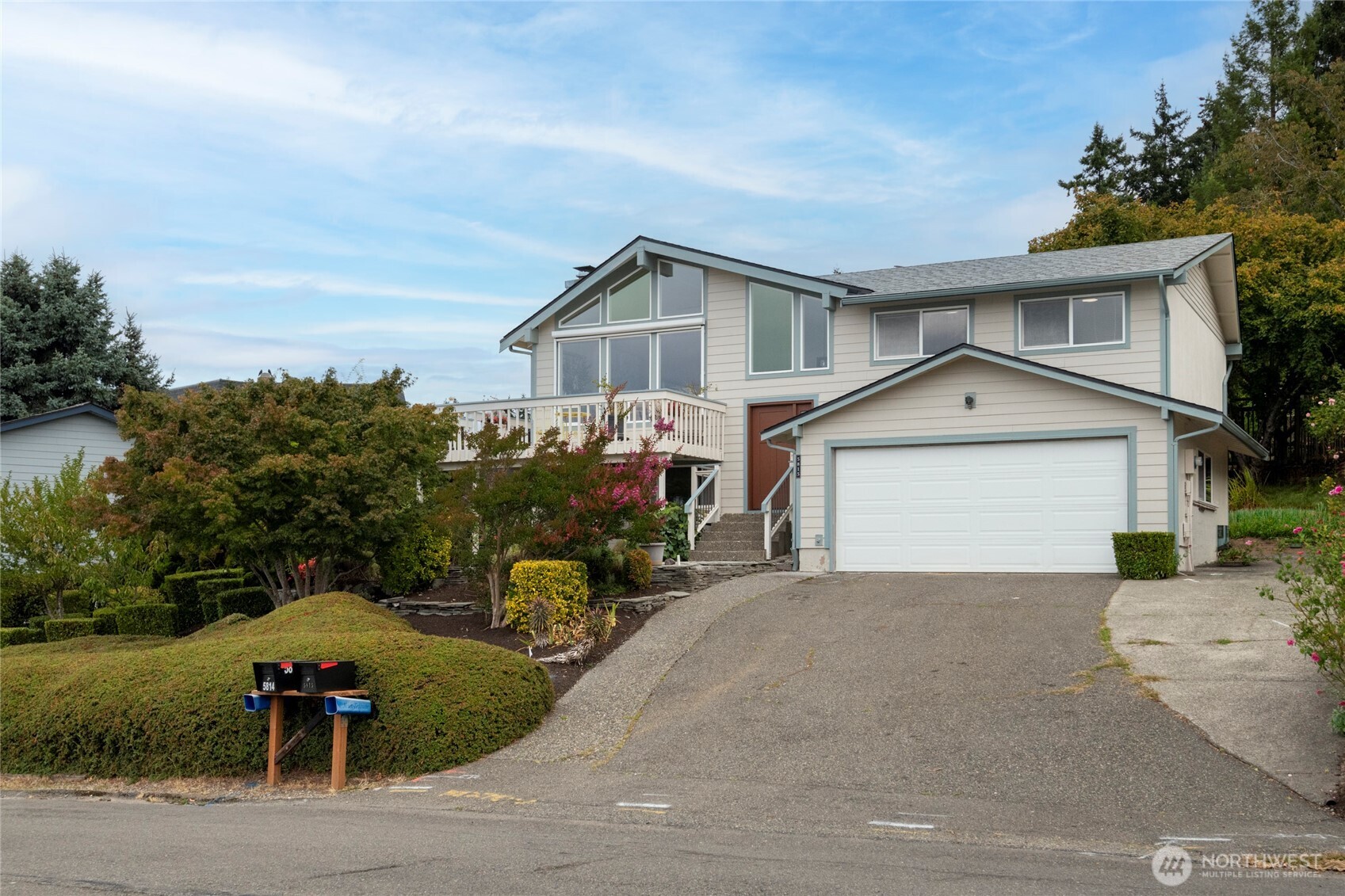 Two-story home with a double garage, elevated deck, and landscaped sloping yard.