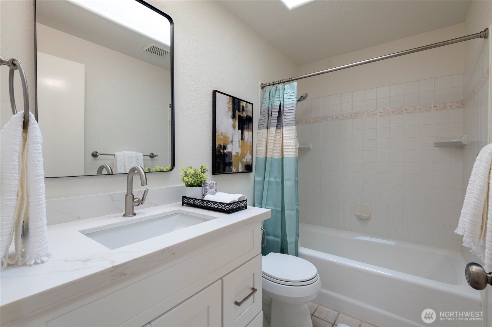 Bathroom with a white vanity, large mirror, tiled tub and shower, and turquoise curtain.