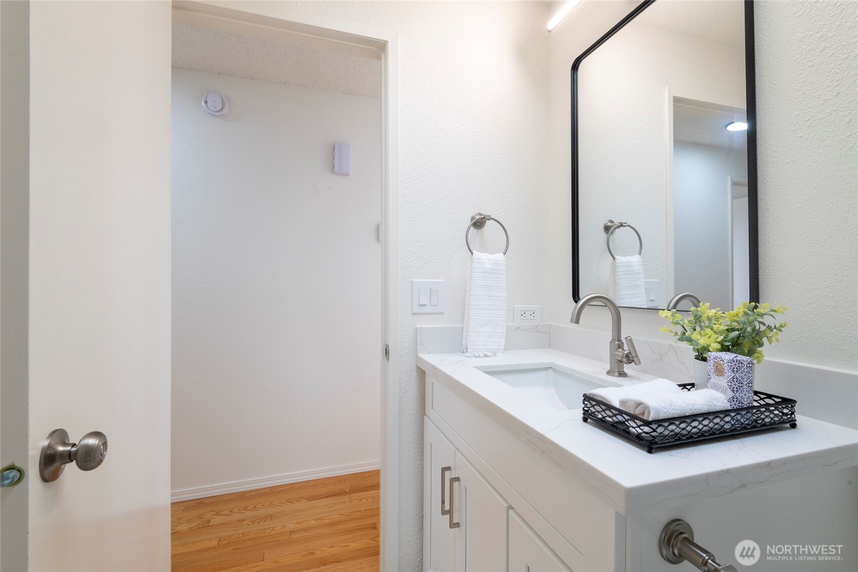 Bathroom vanity with a marble-look countertop, black-framed mirror, and staged towel and plant.