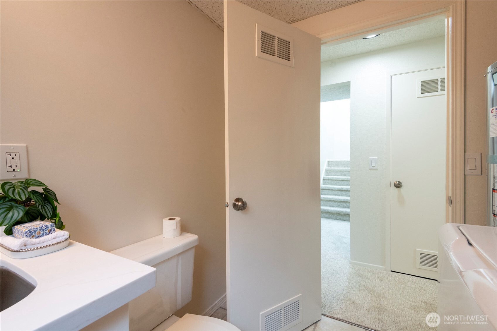 Bathroom with a white sink and toilet; the open doorway looks onto a carpeted hall and stairs.