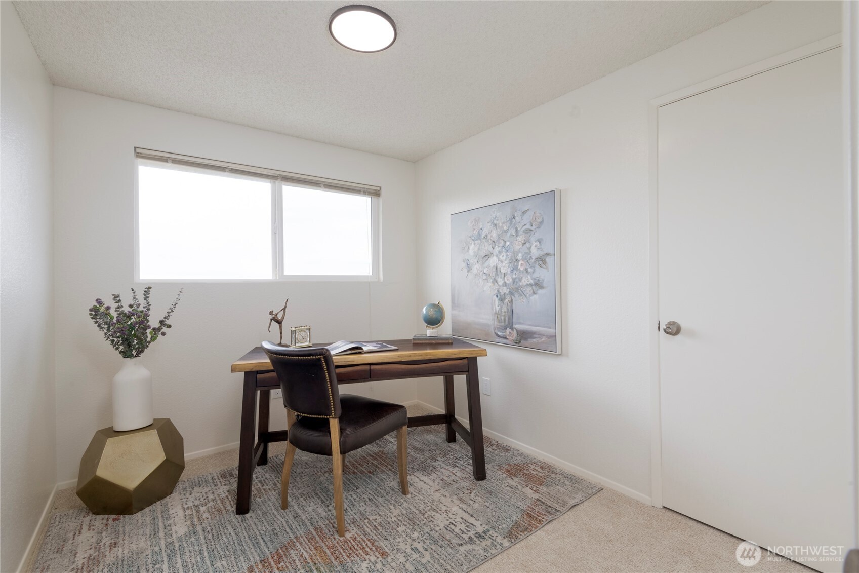 Furnished home office with a wood desk, leather chair, and large window.