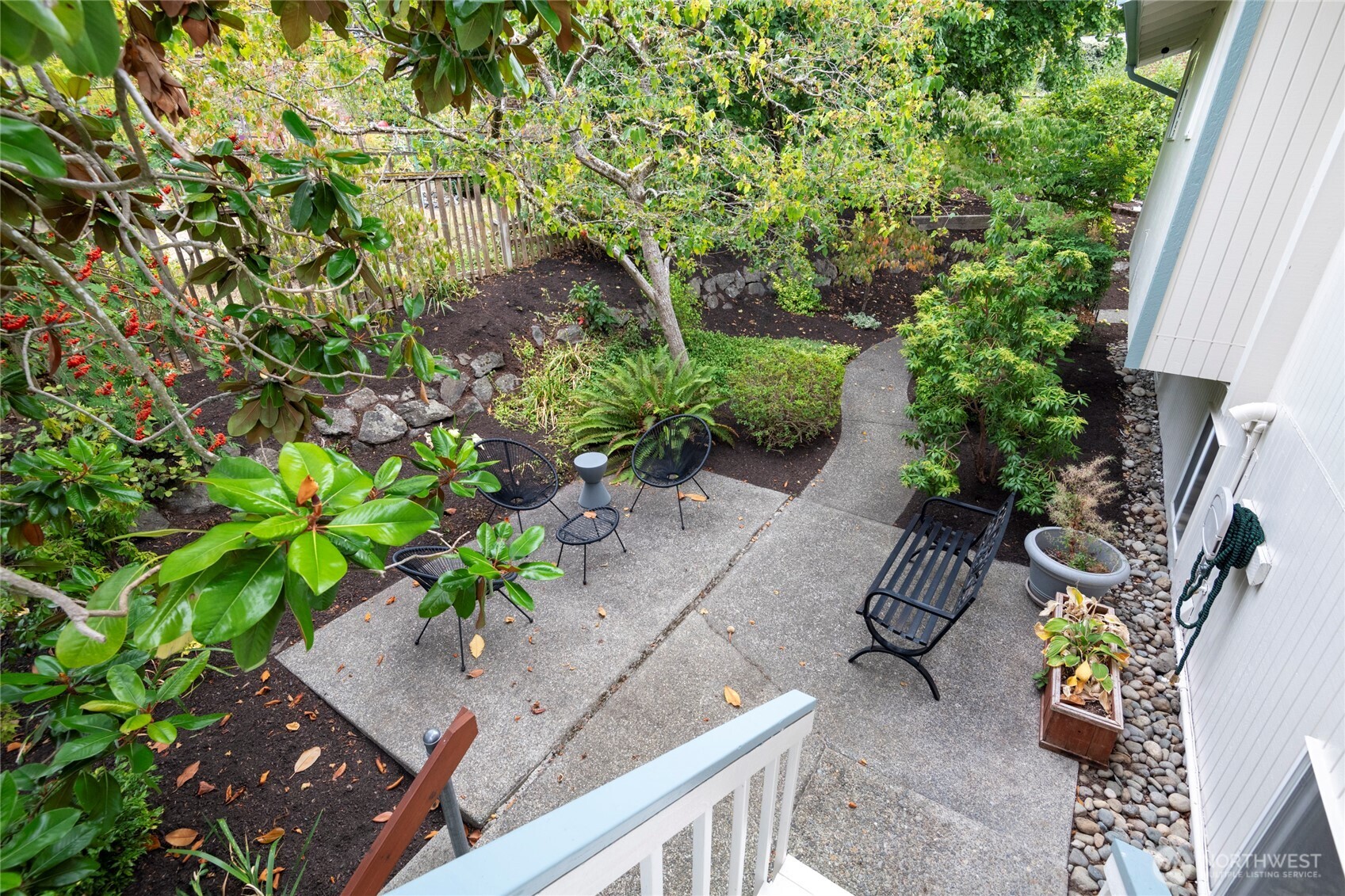 Garden patio with black metal seating, winding paths, and mature trees beside the home.