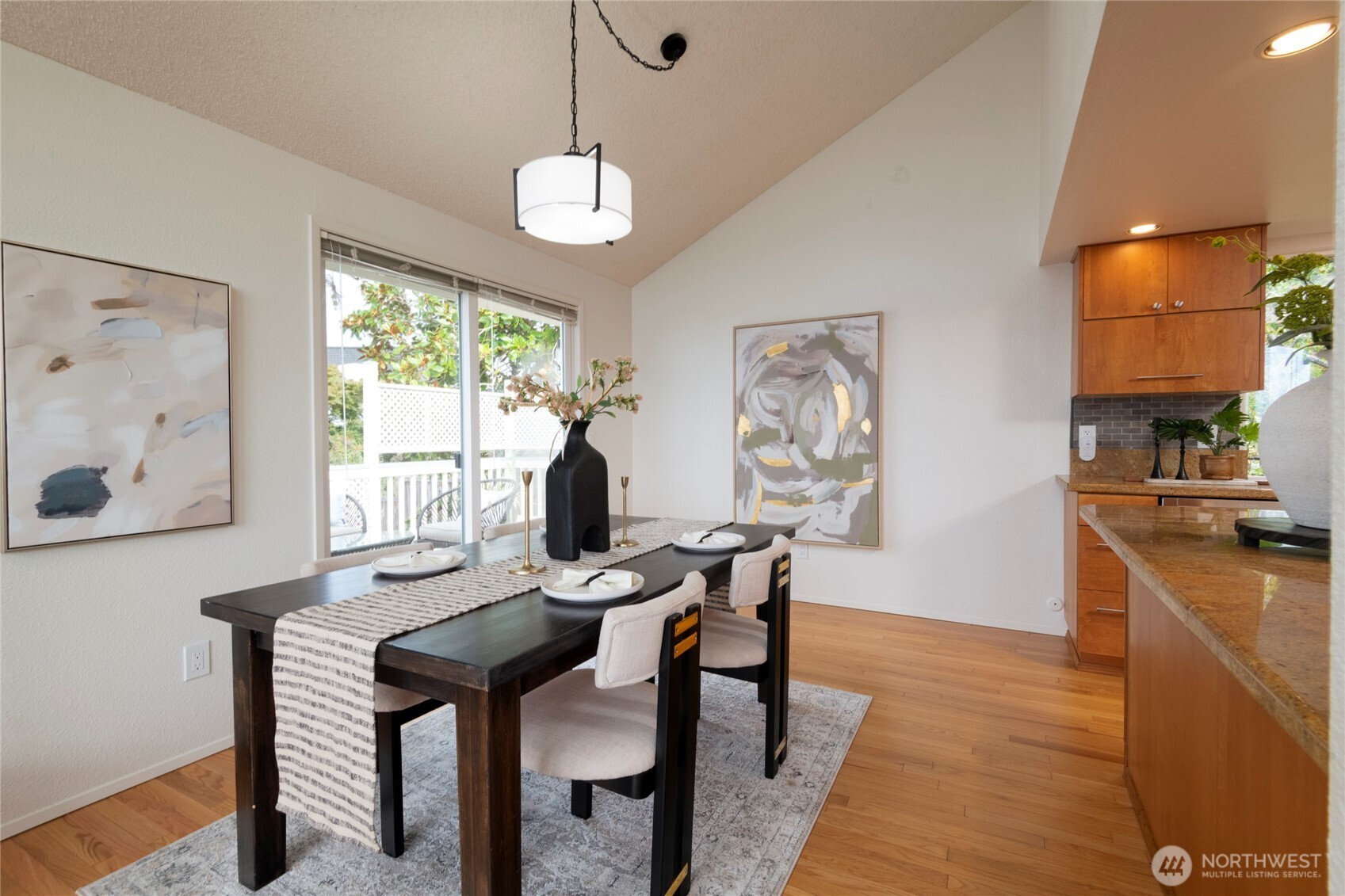 Staged dining room with a set table, abstract art, hardwood floors, and an adjoining kitchen.