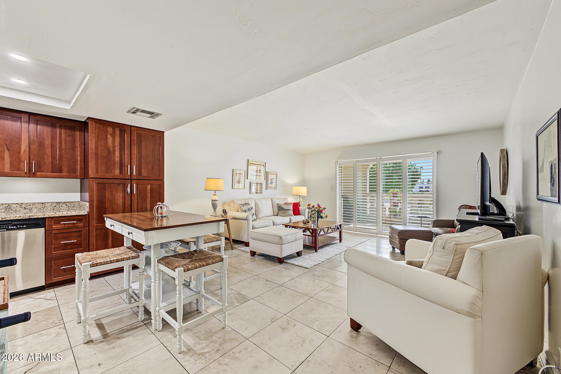 Open-plan kitchen and living room with dark wood cabinets, white sofas, and shuttered sliding glass doors.