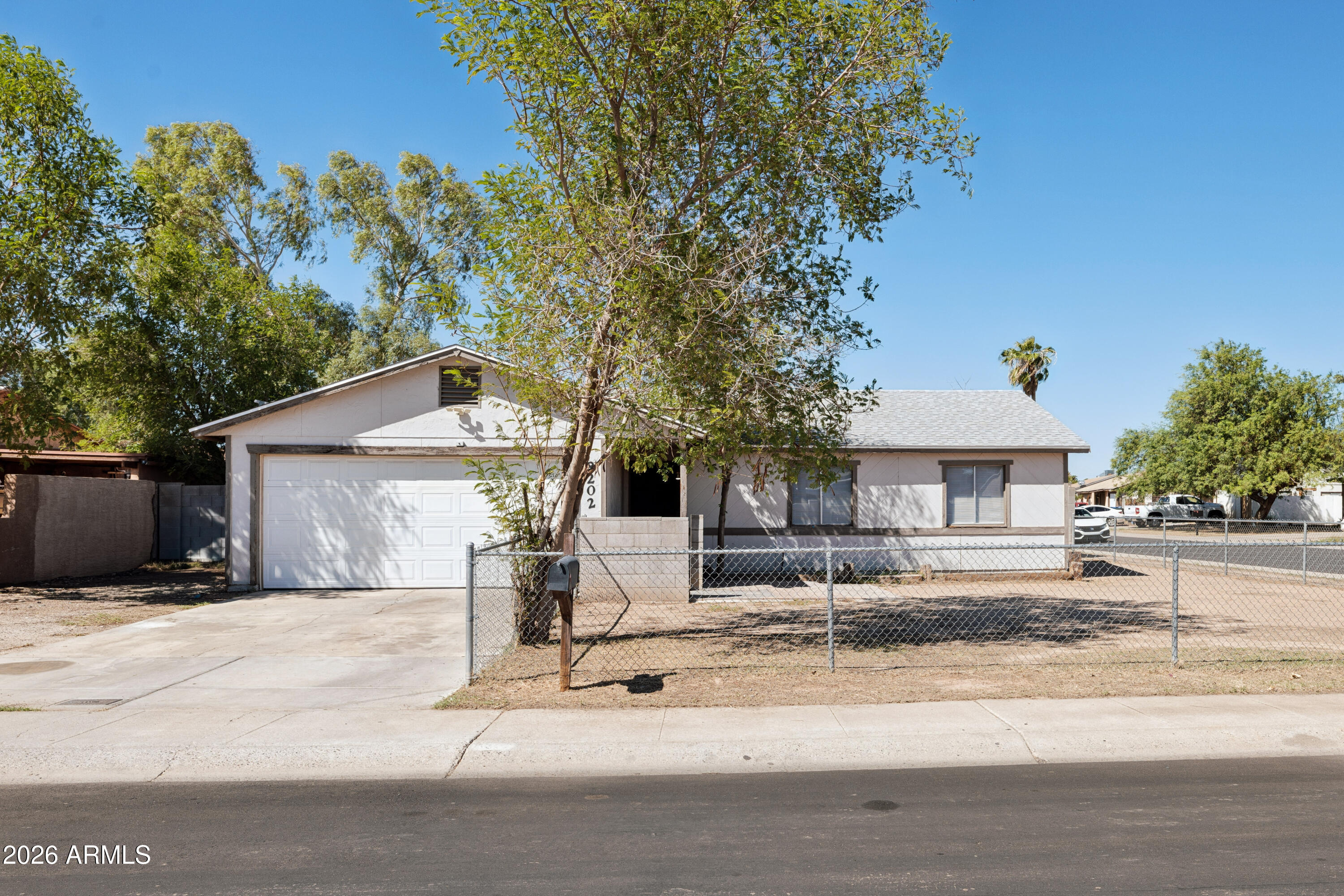 Single-story house with an attached garage, chain-link fence, and mature trees.
