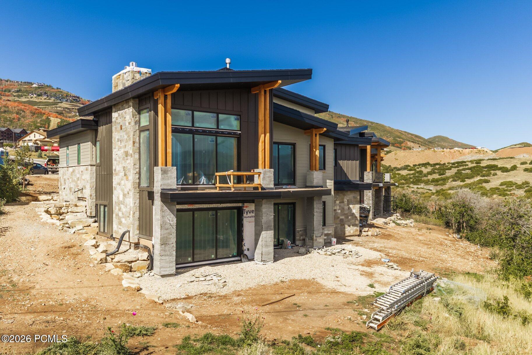 Modern hillside home under construction with stone cladding and dramatic angular rooflines.