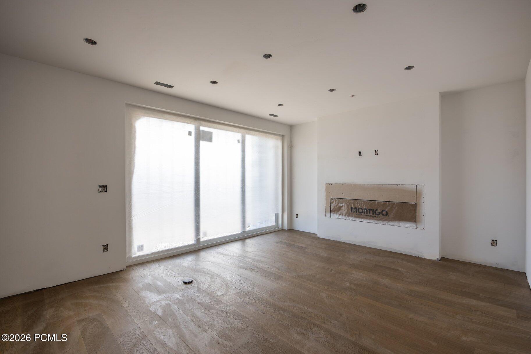 Unfinished room with light wood floors, covered sliding glass doors, and a fireplace insert.