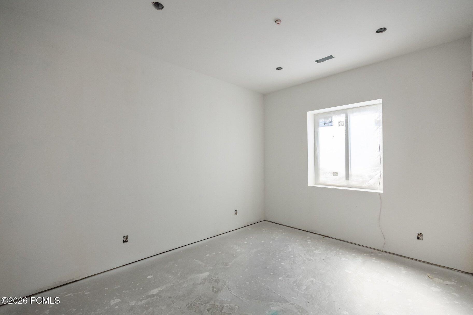 Unfinished empty room with white walls, bare flooring, recessed lights, and a plastic-covered window.