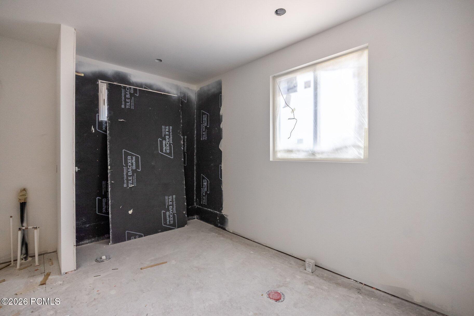 Unfinished bathroom with black shower backer panels, exposed plumbing, and a plastic-covered window.