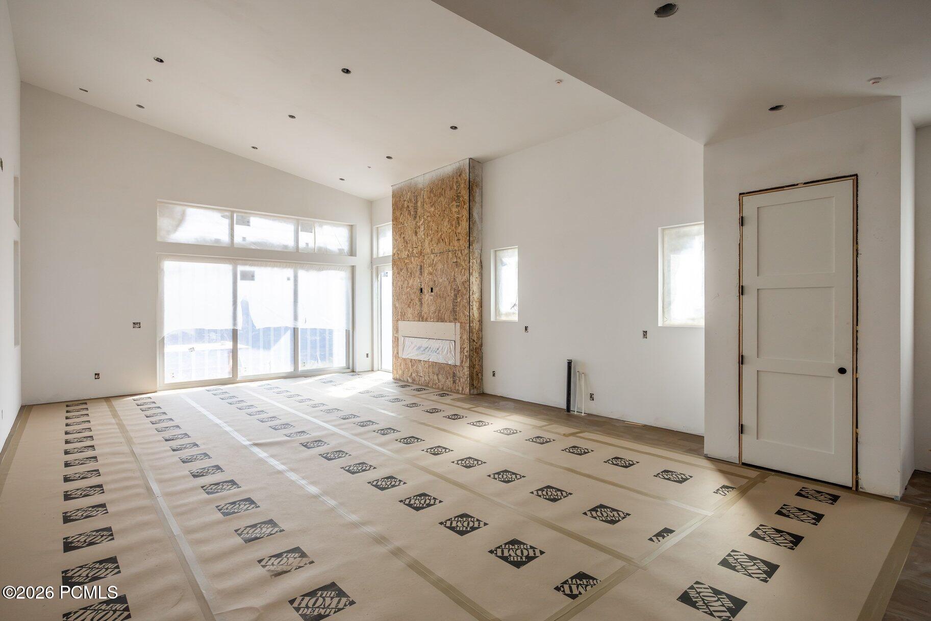 Unfinished living room with a tall fireplace surround, large windows, and protective floor covering.