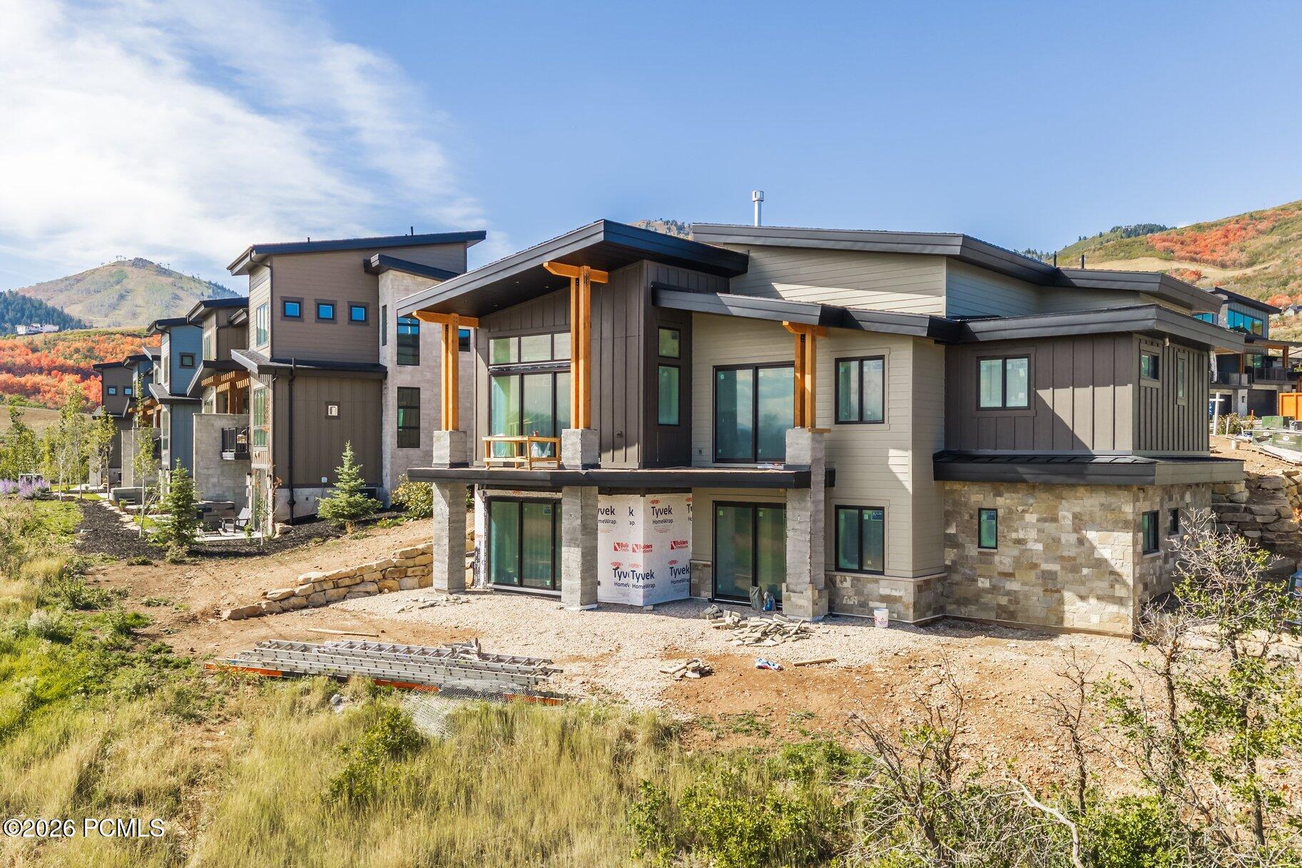 Modern hillside home under construction with stone veneer and timber porch supports, backed by autumn mountains.