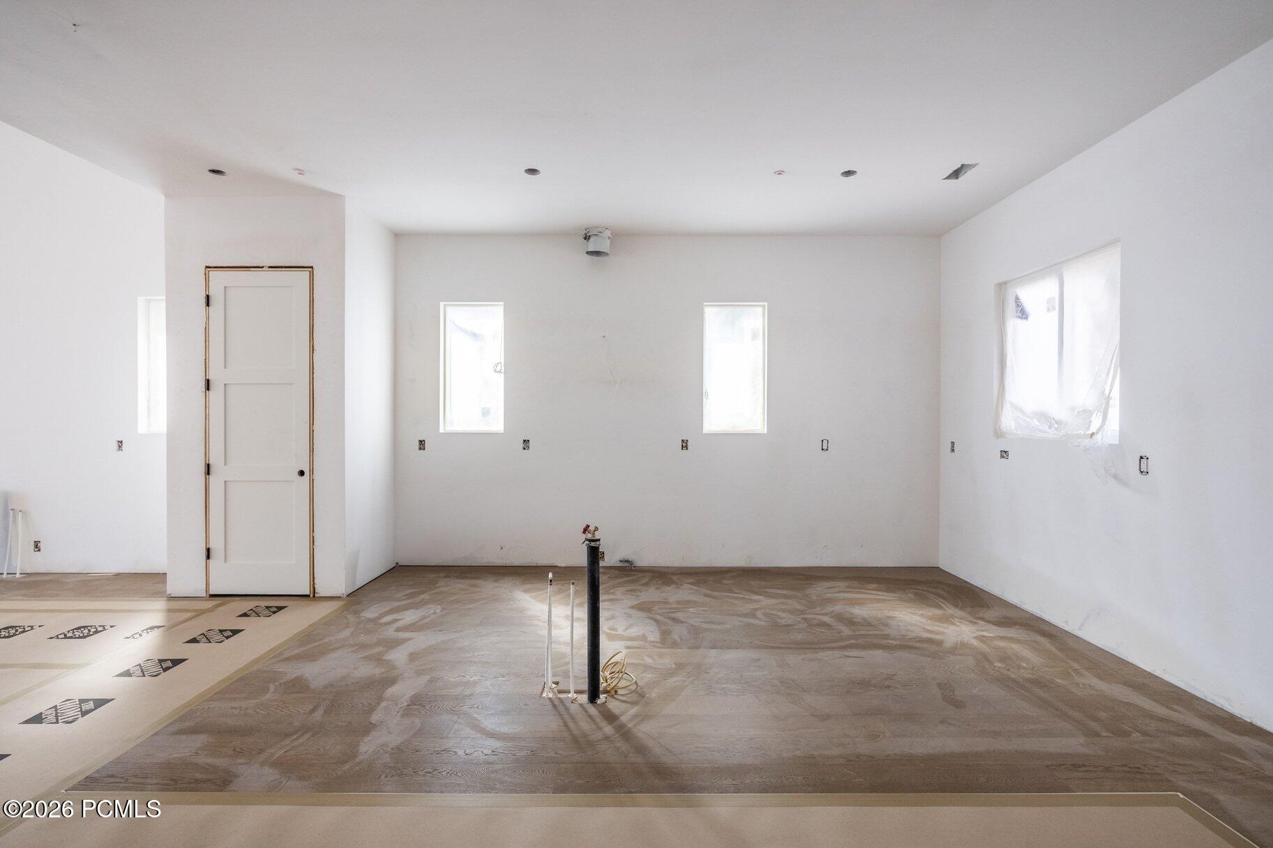 Unfinished room with exposed plumbing, bare walls, and several windows.