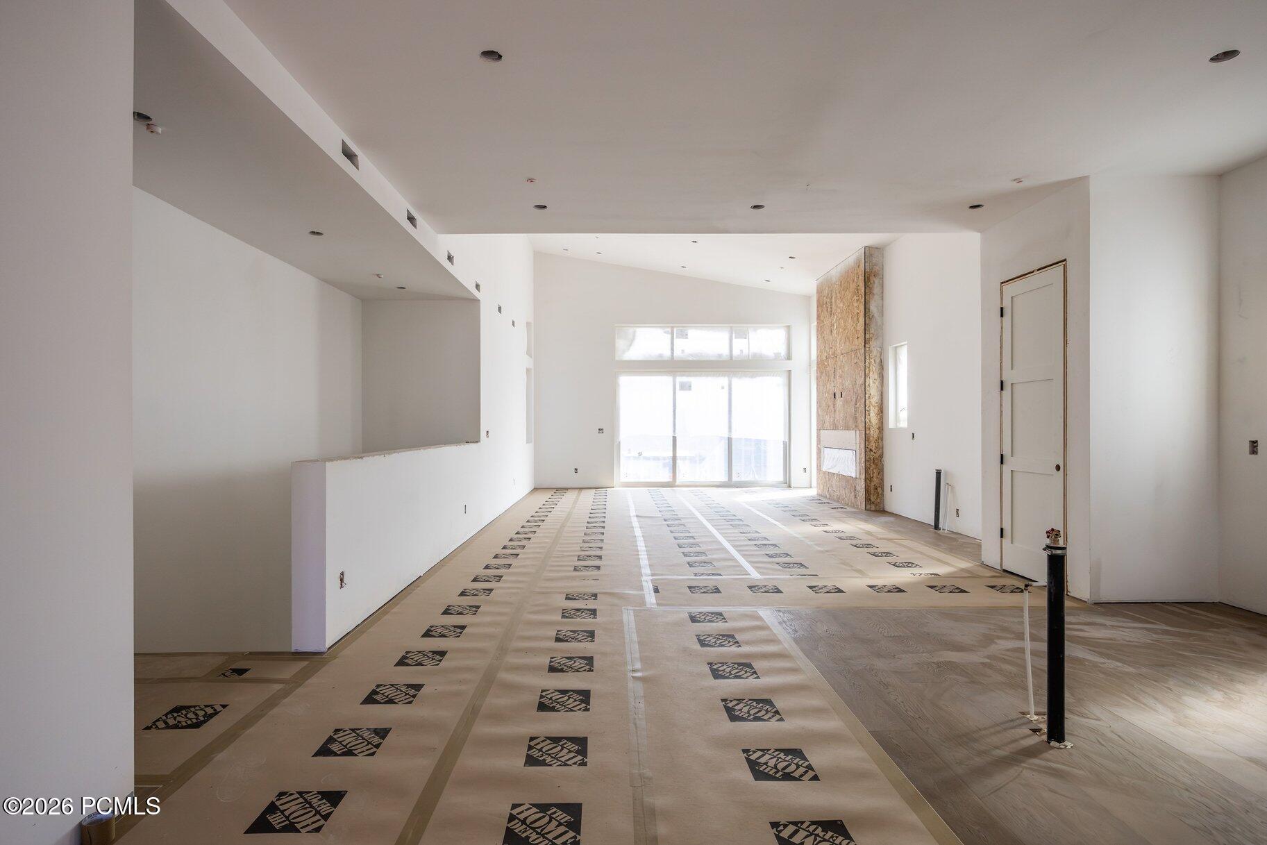 Unfinished great room with large windows, a stone fireplace, and protective floor covering.