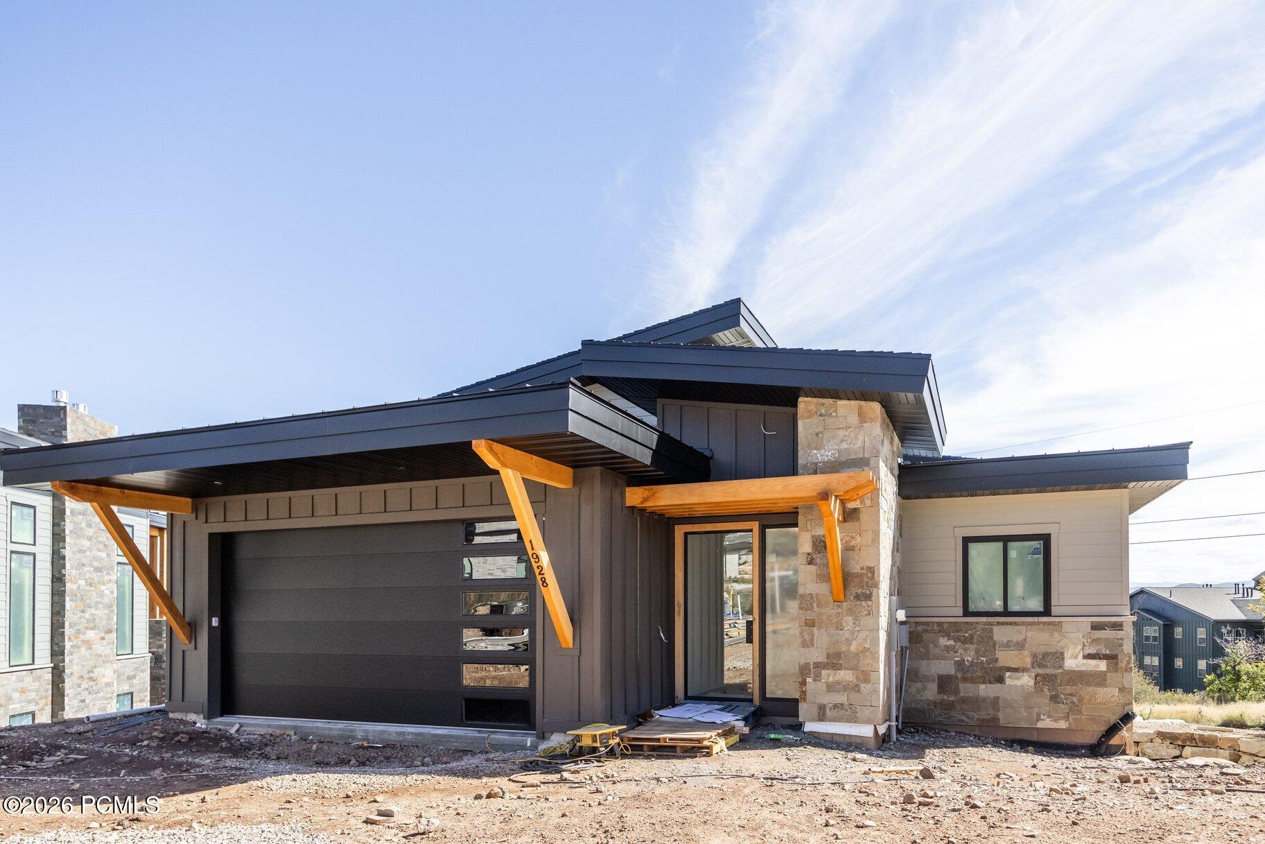 Modern home under construction with dark siding, stone accents, and timber porch supports.