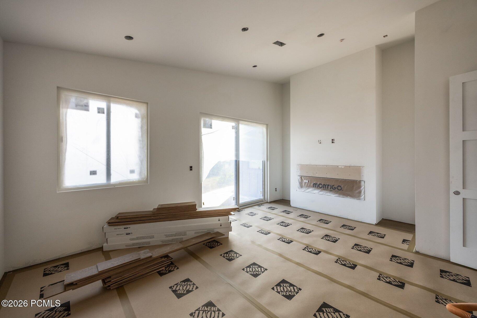 Unfinished living room with a fireplace insert, windows, and flooring materials on the floor.