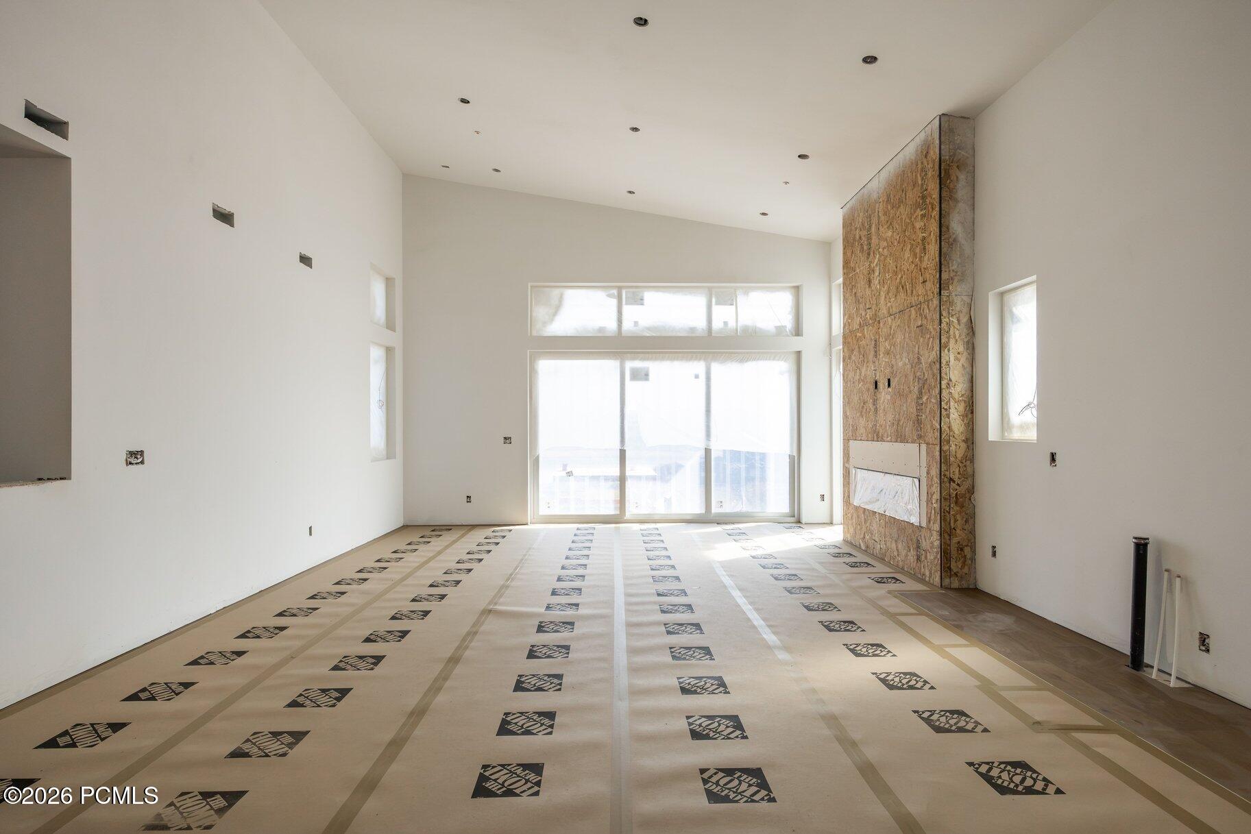Unfinished living room with a tall stone fireplace surround, large windows, and protective floor covering.