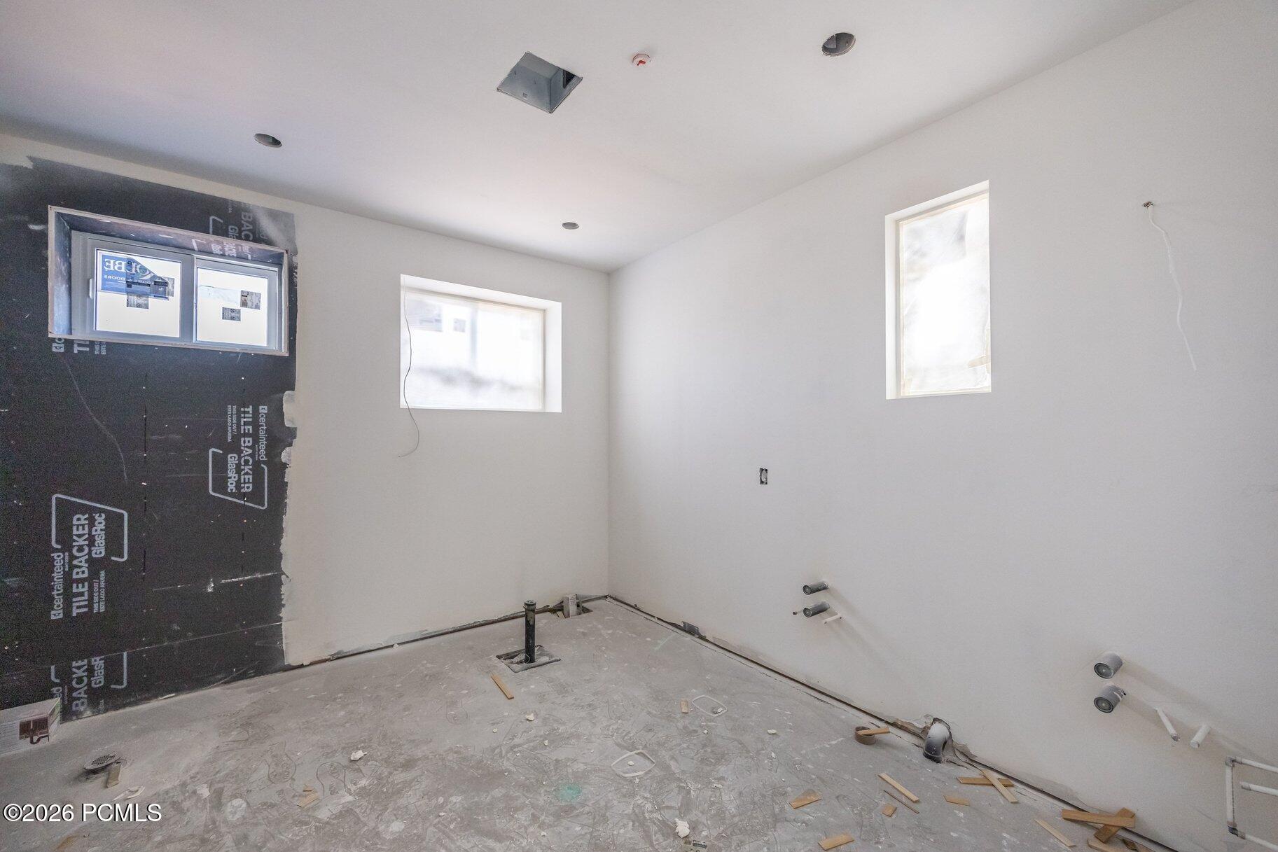 Unfinished bathroom with exposed plumbing, two windows, and tile backer board on one wall.