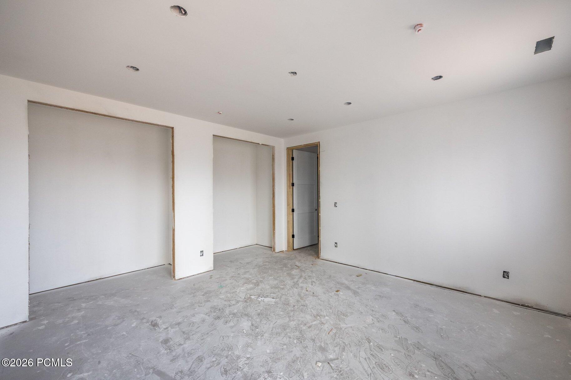 Unfinished interior room with white drywall, exposed framing, recessed lights, and a dusty concrete floor.