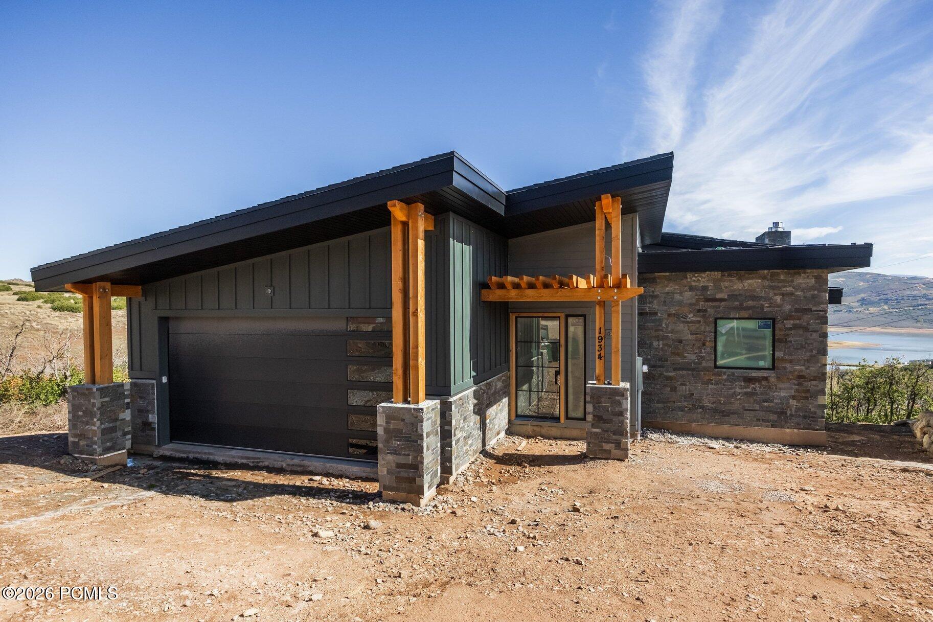 Modern dark-sided home with stone veneer, timber supports, and water visible in the distance.