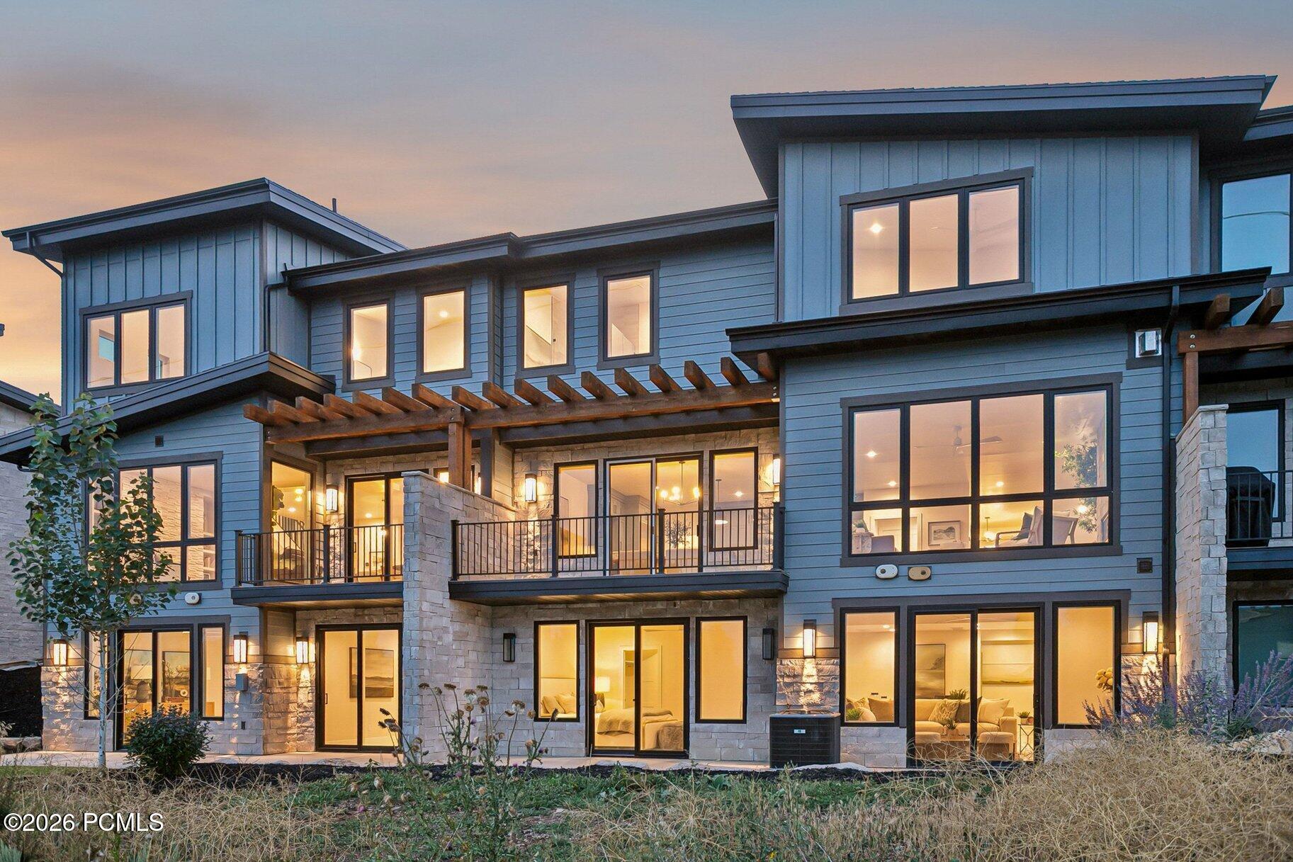 Modern multi-level home with blue siding, stone accents, and a timber pergola at dusk.
