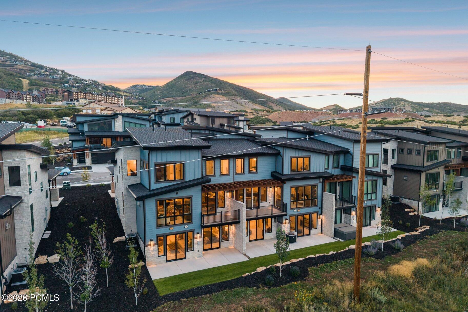 Modern multi-story homes with warm-lit windows, landscaped yards, and mountain views at sunset.
