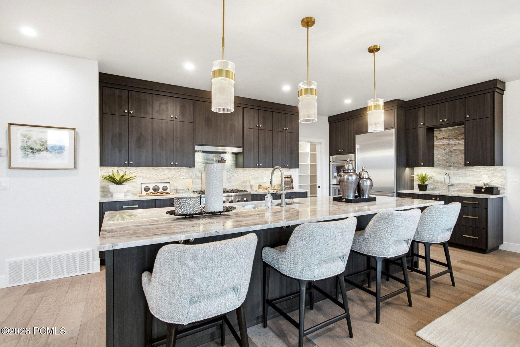 Modern kitchen with dark cabinetry, a large stone island, and brass pendant lights.