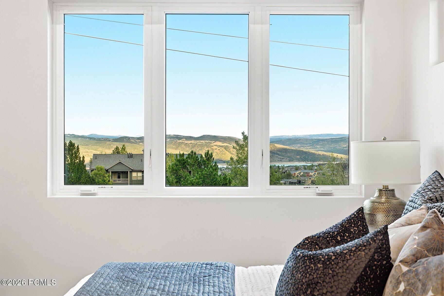 Bedroom with a wide mountain and lake view through three large windows.
