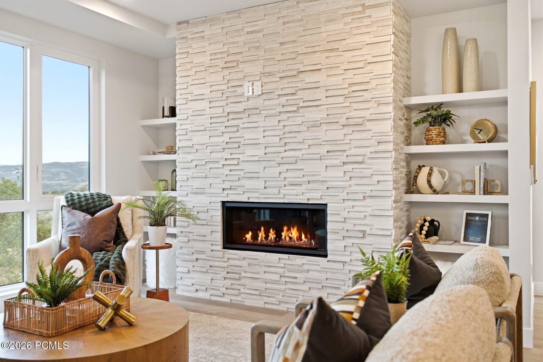 Living room with a tall white stone fireplace, built-in shelves, and windows overlooking mountains.