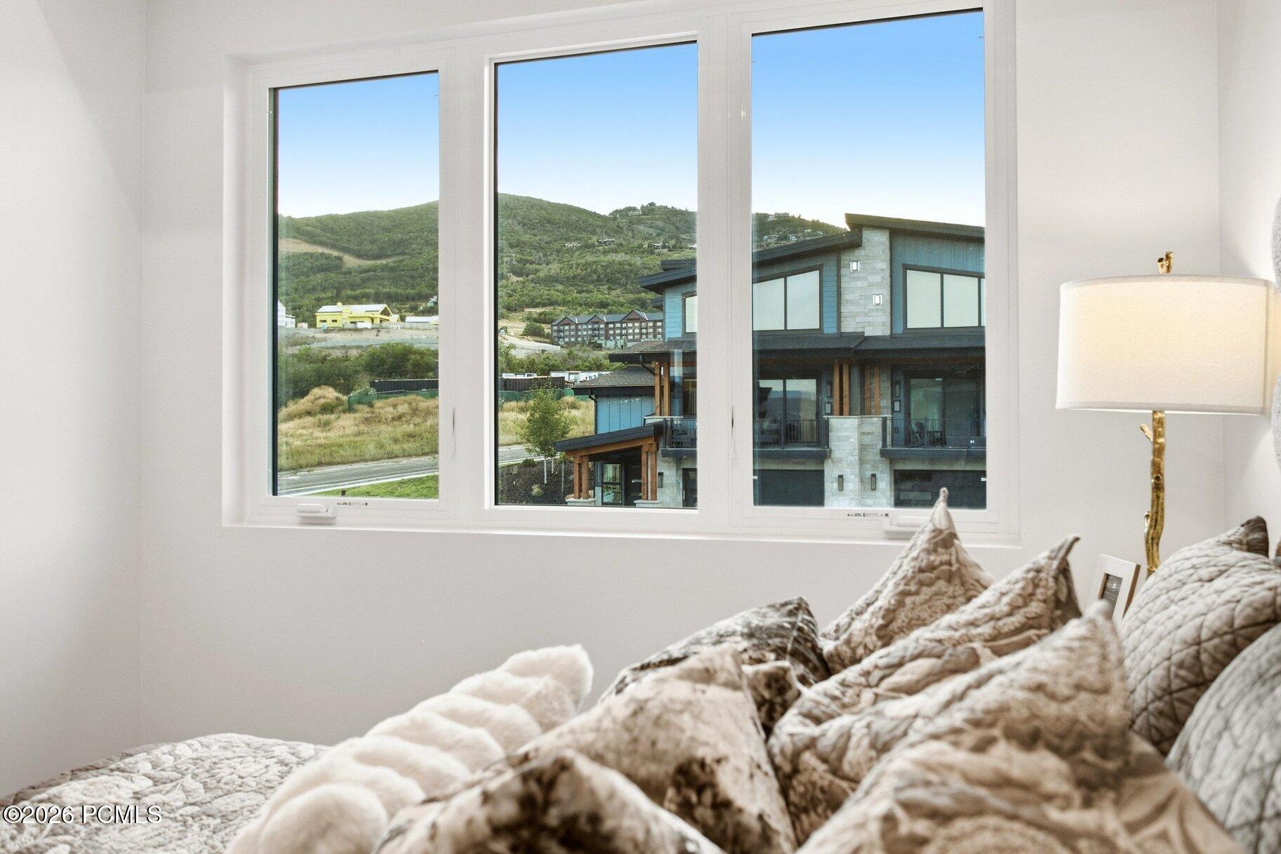 Bedroom with large windows overlooking green hills and a modern neighboring home.