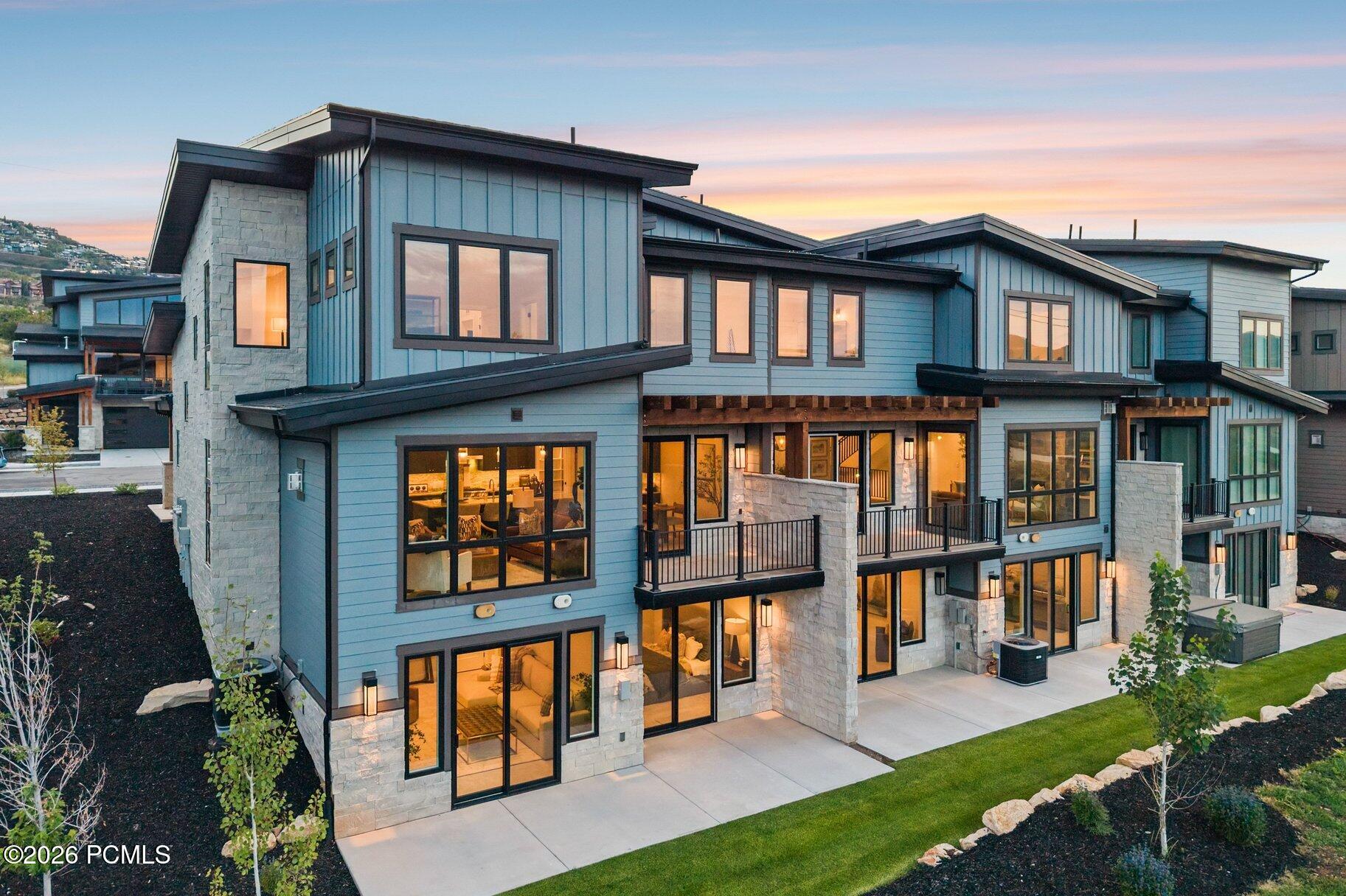 Modern multi-level home with blue-gray siding, stone accents, and illuminated windows at dusk.
