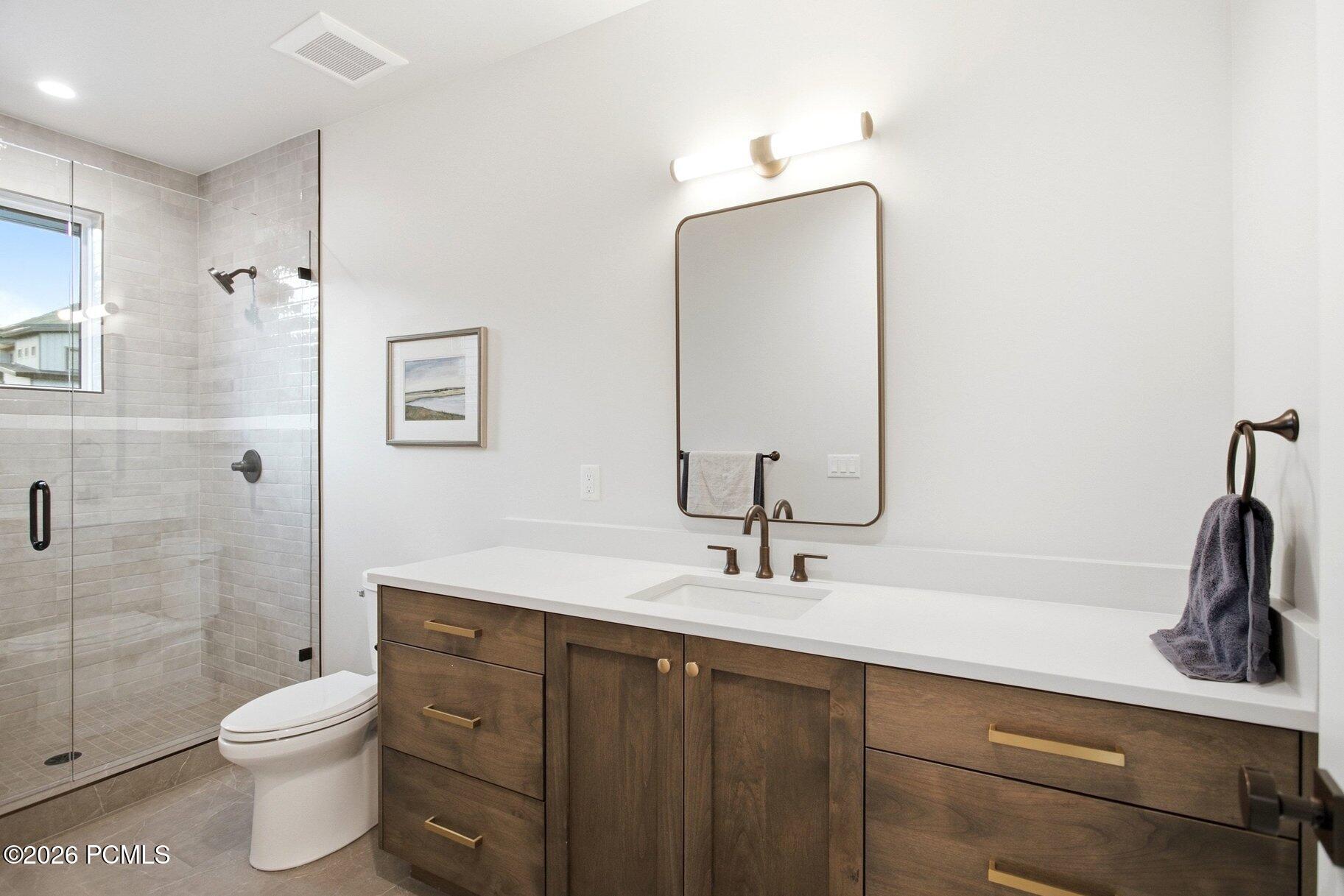 Bathroom with a glass walk-in shower and long wood vanity beneath a large mirror.