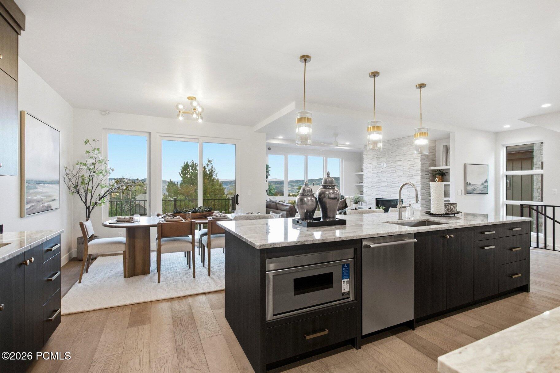 Open-plan kitchen with a large marble island and dining area overlooking trees and distant hills.