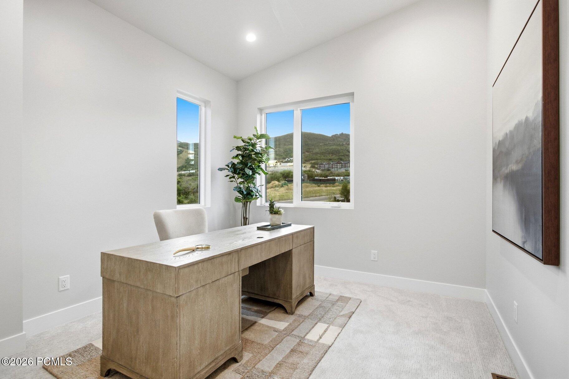 Home office with a wood desk and windows overlooking green hills.
