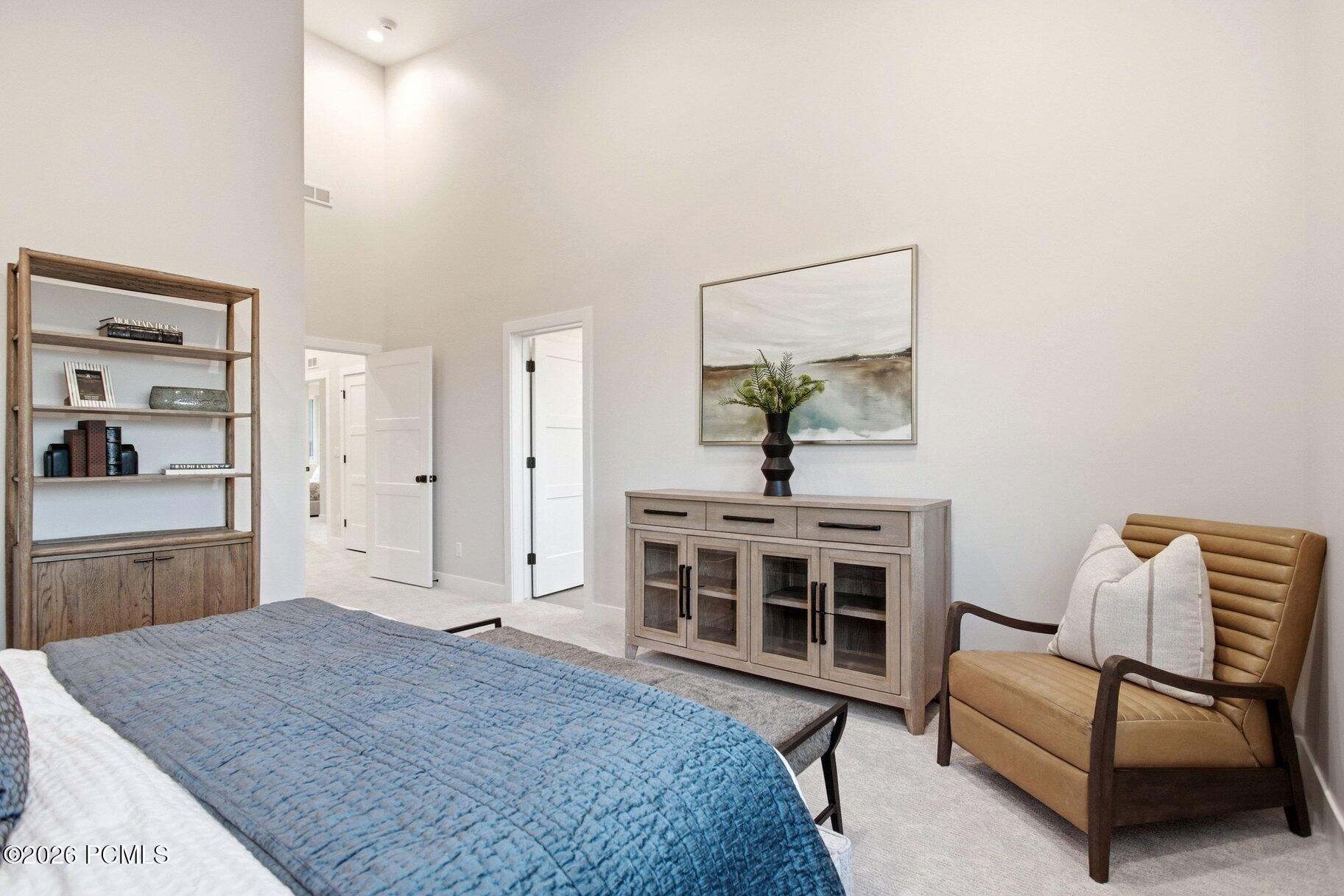 Bedroom with a blue quilted bed, high ceiling, and tan leather armchair.
