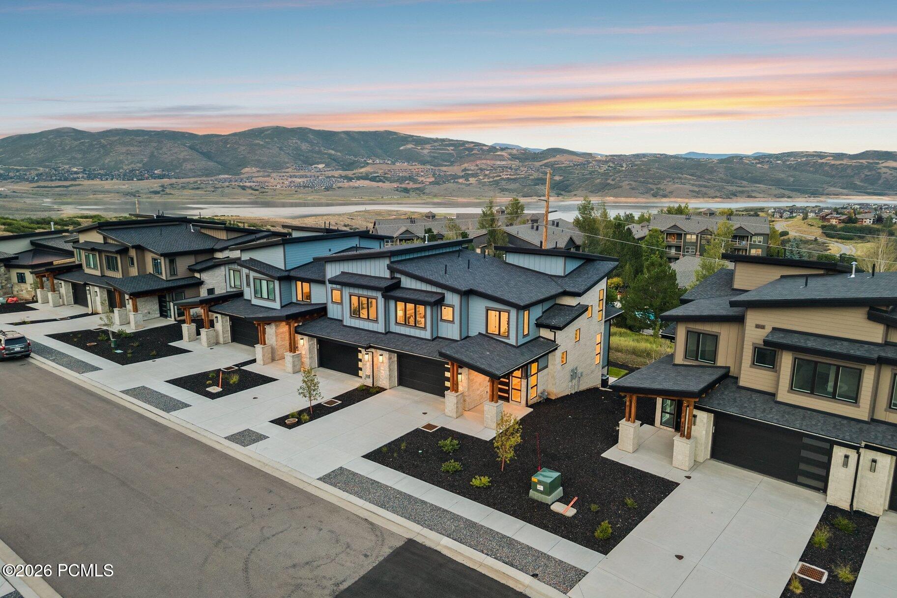Modern homes with dark garages overlook a lake and mountains at sunset.