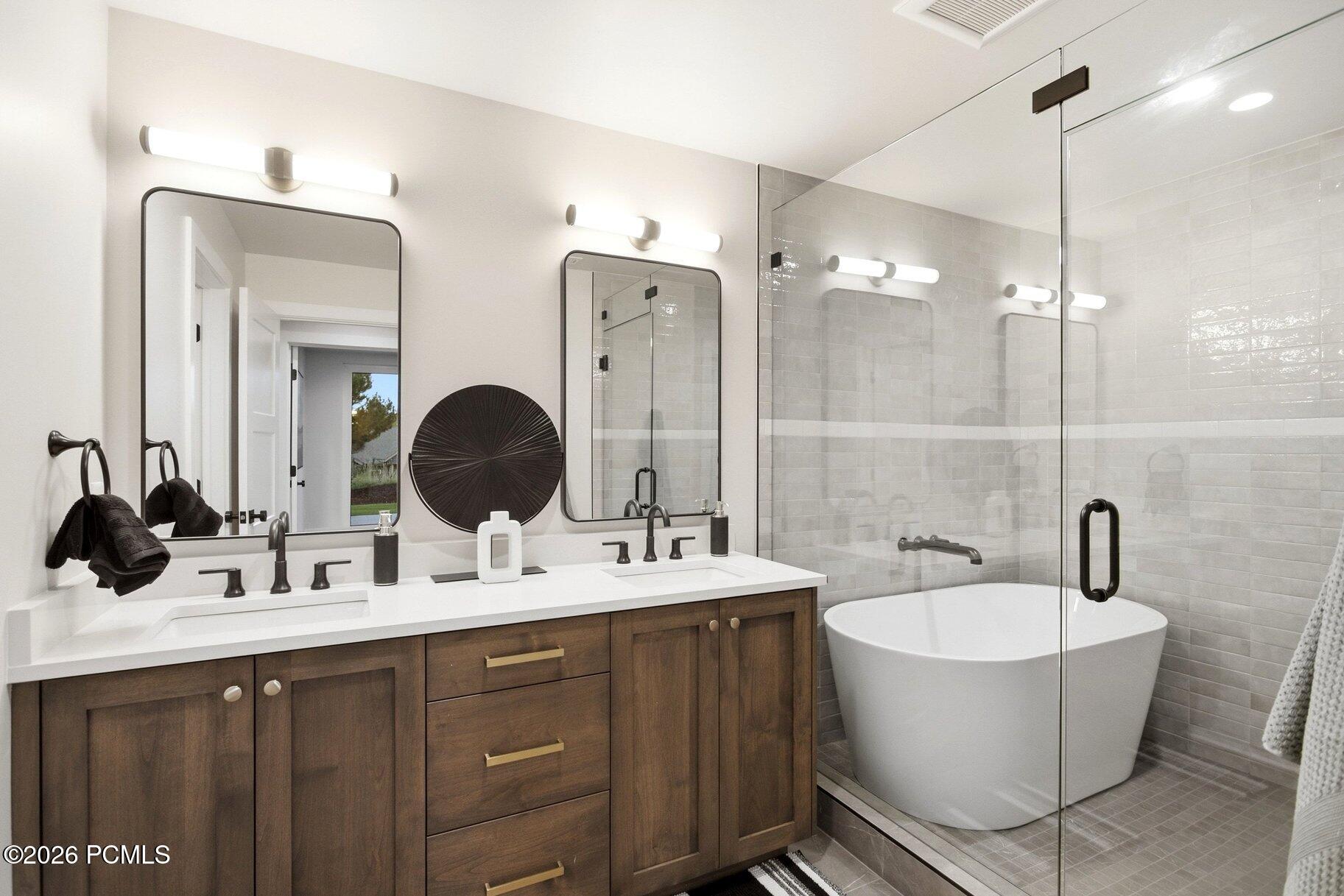Bathroom with a double vanity and glass shower beside a freestanding soaking tub.